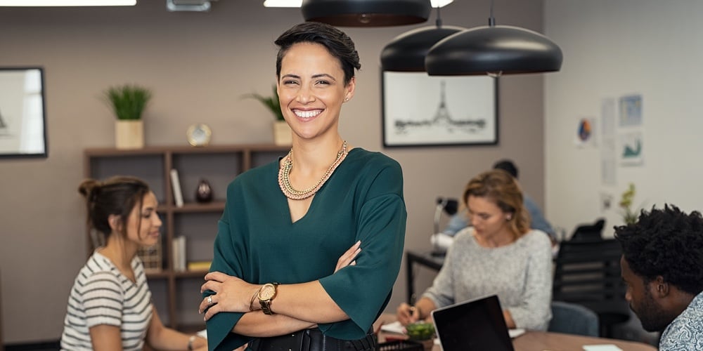 Portrait of sucher colleagues working in background at ofcessful business woman standing with fice.