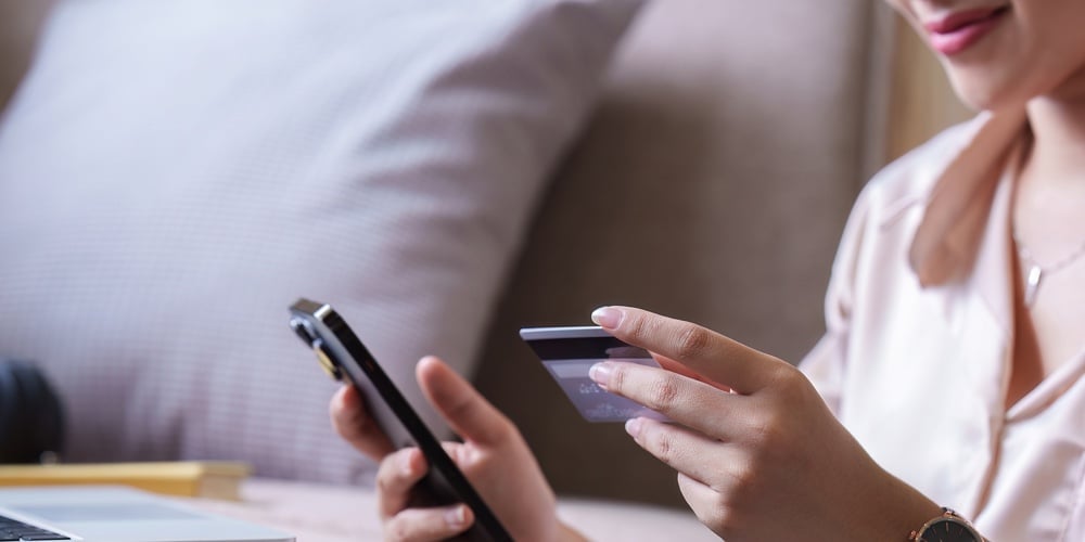 Pretty Asian Woman Shopping Online With Credit Card And Smartphone While Sitting On Sofa At Home