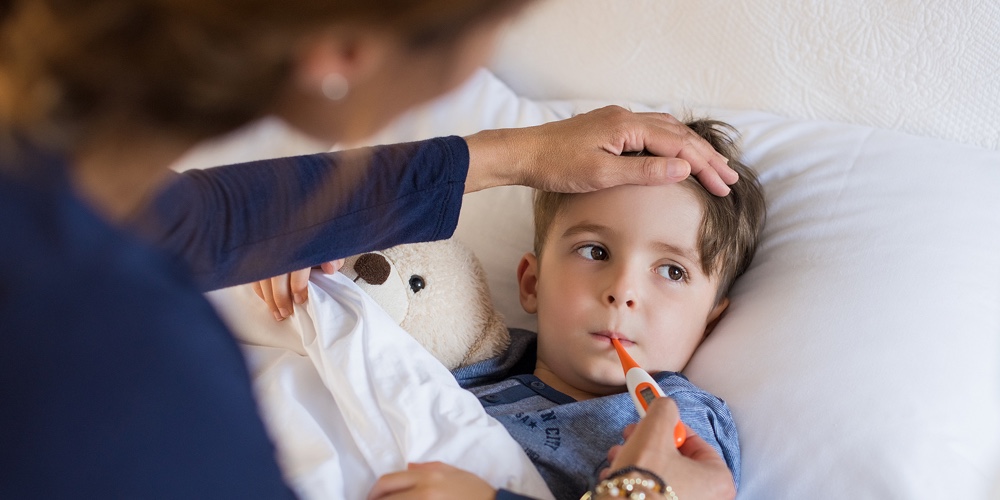 Sick boy with thermometer laying in bed and mother hand taking temperature. Mother checking temperat