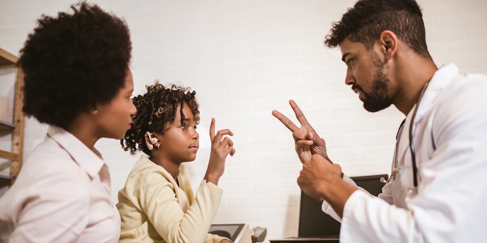 Smiling Deaf African American Girl With Ear Implant At Doctor’s Office.