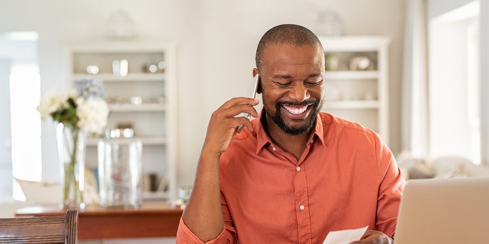 Smiling african man using laptop at home while checking home finance. Happy mature man looking at in