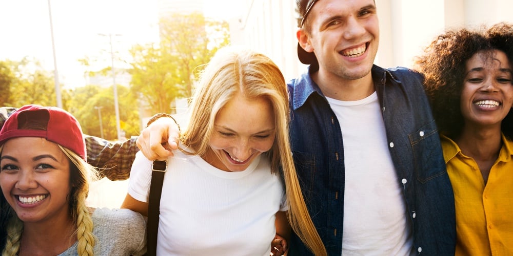Smiling happy young adult friends arms around shoulder walking outdoors