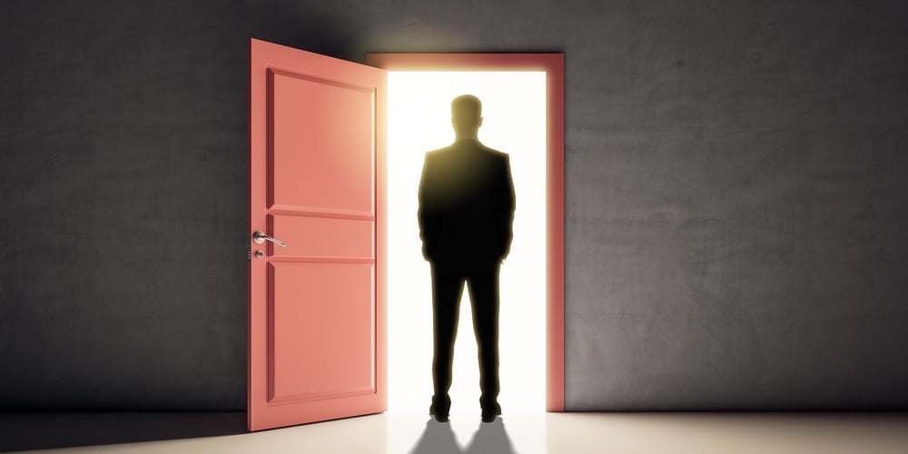 Successful Business Man Standing In Front Of Bright Door In Concrete Interior With Shadow On Floor.