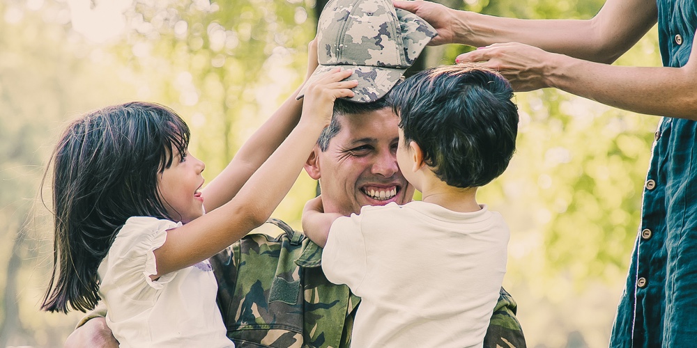 Two Happy Kids And Their Mom Meeting And Hugging Military Dad In Camouflage Uniform Outdoors. Family