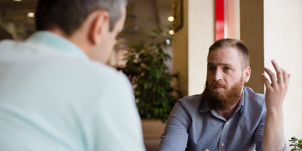 Two Men Discussing Difficult Issues With Emotions During Coffee Break In Cafe Talking About Problems