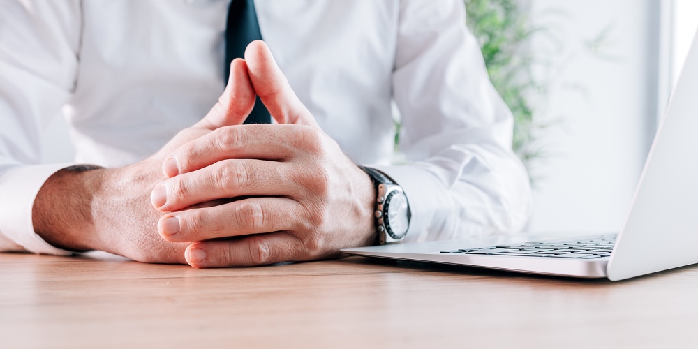 Uncomfortable Businessman With Hands Clasped On Office Desk