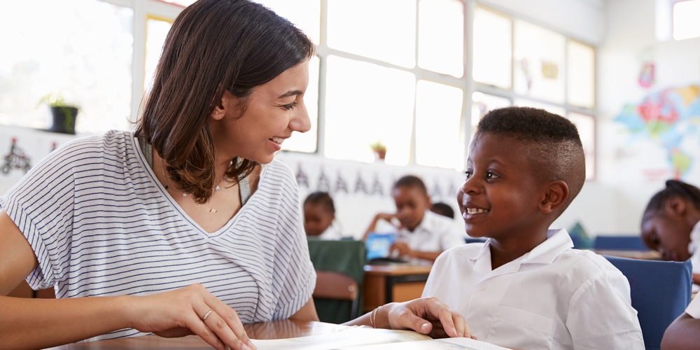 Volunteer teacher helping schoolboy at his desk