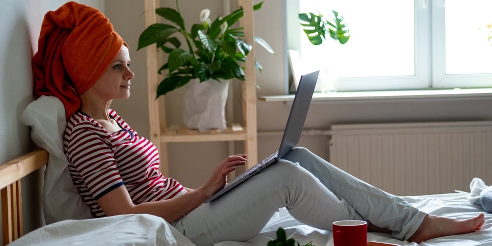Woman With Orange Towel On Head Is Working Office Work Remotely From Home On Bed. Using Computer. Di