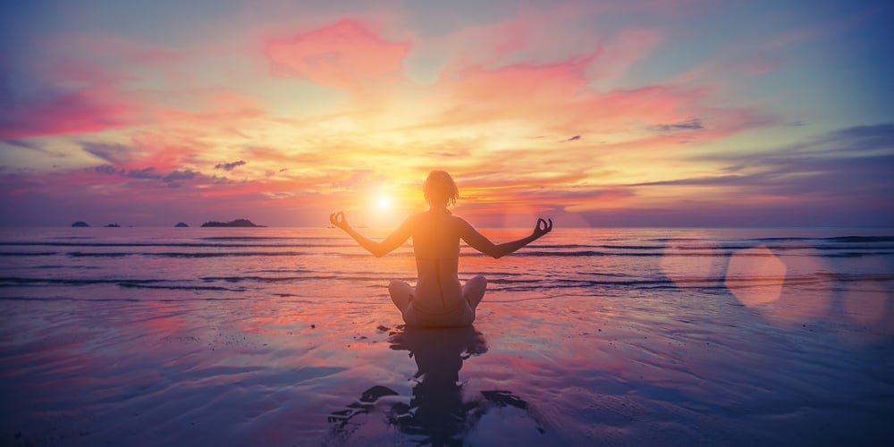 Woman doing meditation near the ocean beach. Yoga silhouette.