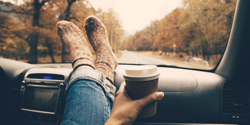 Woman feet in warm socks on car dashboard. Drinking take away coffee on road. Fall trip. Rain drops