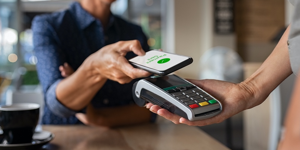 Woman paying bill through smartphone using NFC technology in a restaurant. Satisfied customer paying