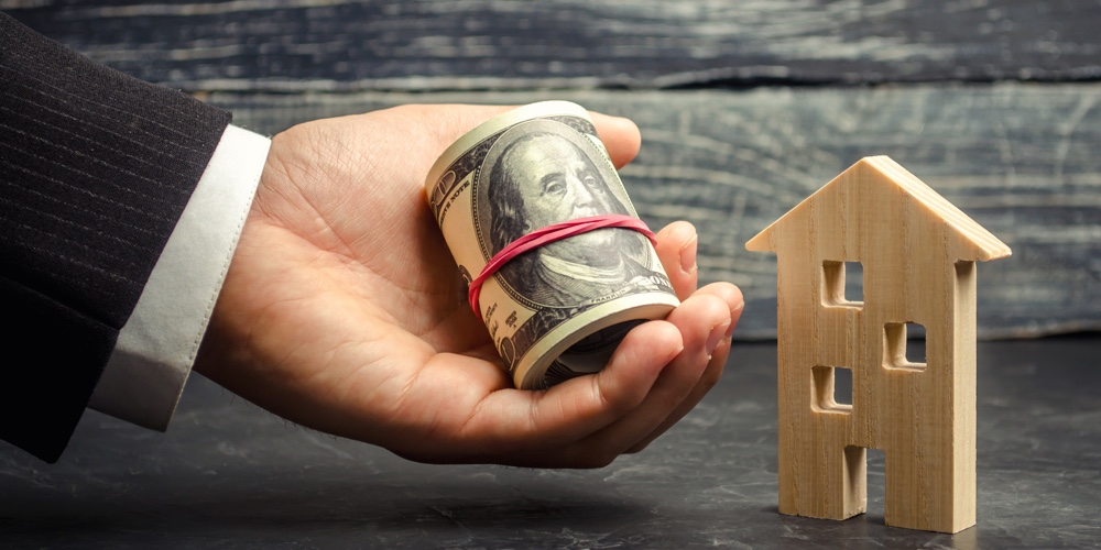 Wooden House And Money In Hand. A Loan Secured By Real Estate. Home Renovation And Repair. Warm Loan