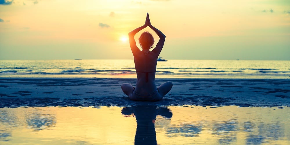 Yoga woman sitting in lotus pose on the beach during sunset