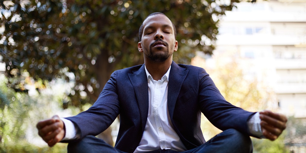 Young American African Businessman In Informal Clothes Meditating In Lotus Pose Taking A Deep Breath