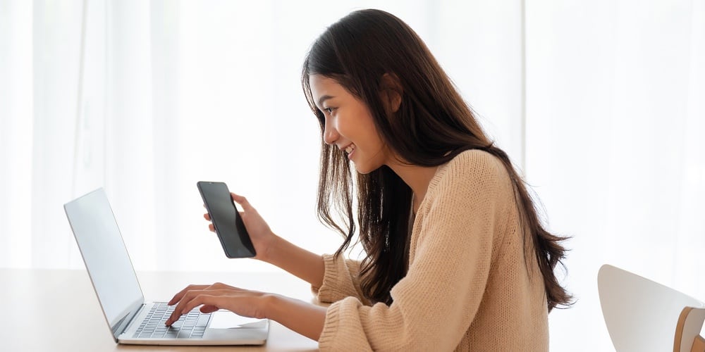 Young Asian Woman Happy Working On Computer Laptop And Hand Typing Chat Message On Mobile Smartphone