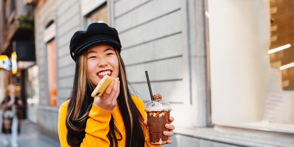 Young Asian Woman Sending Voice Messages With An Online Messaging App On Her Smartphone While Having