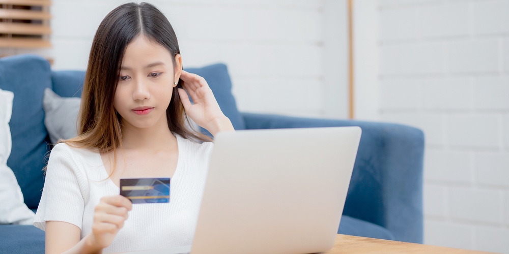 Young Asian Woman Sit On Sofa Using Laptop Computer Shopping Online With Credit Card Buying To Inter