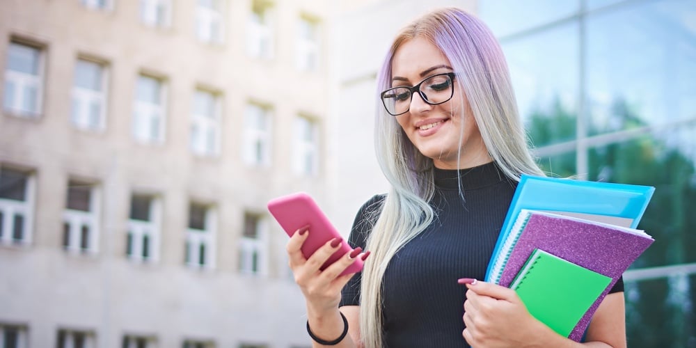 Young Student Girl Using Smart Mobile Phone To Check Social Media Platforms – Millennial Influencer|Horizontal Shot Of Pretty Smiling Woman Types On Smart Phone