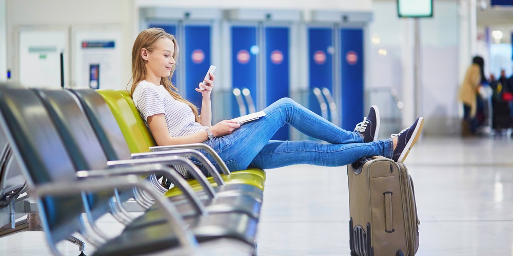 Young Travelerin International Airport Checking Her Mobile Phone While Waiting For Her Flight
