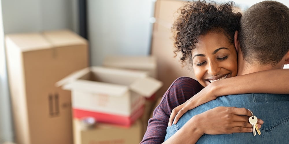 Young african woman holding home keys while hugging boyfriend in their new apartment after buying re
