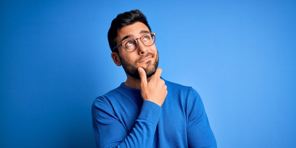 Young handsome man with beard wearing casual sweater and glasses over blue background Thinking worri