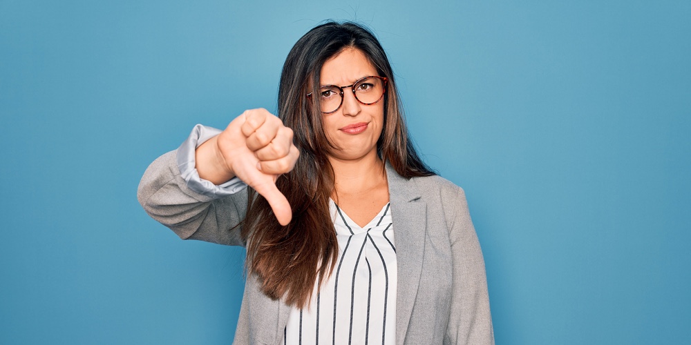 Young hispanic business woman wearing glasses standing over blue isolated background looking unhappy