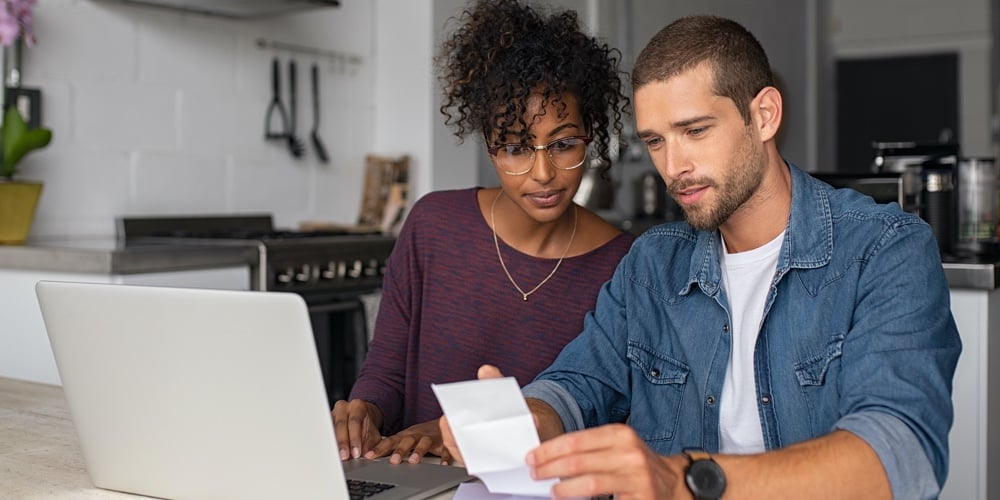 Young multiethnic couple checking bills while managing accounts on home banking app. Serious casual