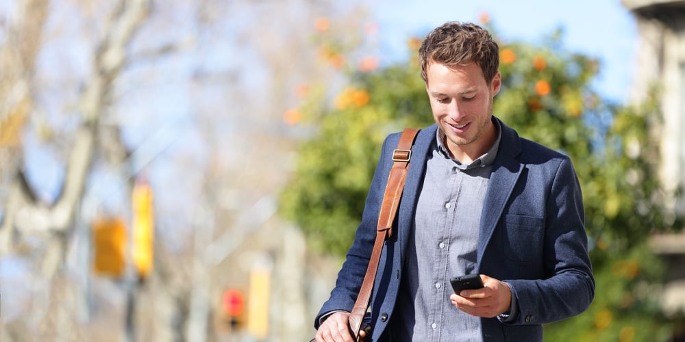 Young urban businessman professional on smartphone walking in street using mobile phone app texting