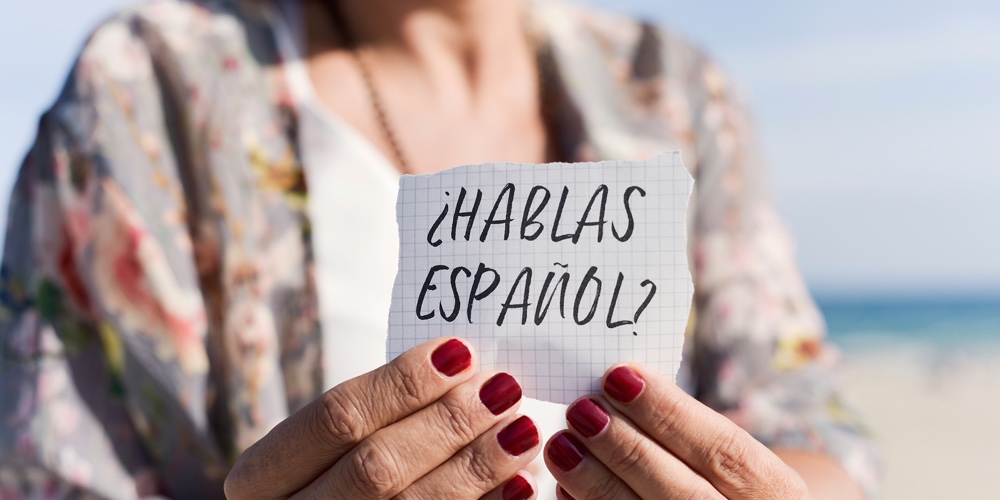 closeup of a caucasian woman outdoors showing a piece of paper with the question hablas espanol