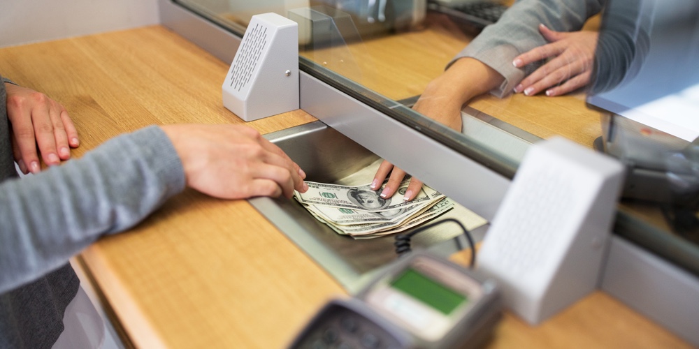 people, withdrawal, saving and finance concept – clerk giving cash money to customer at bank office