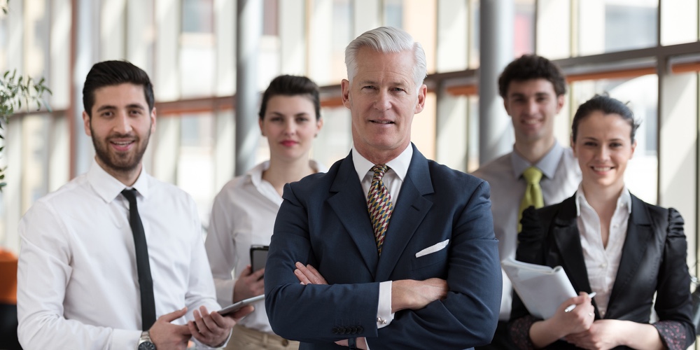 portrait of senior businessman as leader  at modern bright office interior, young  people group in b