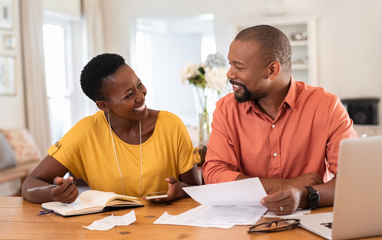Mature couple sitting and managing expenses at home. Happy african man and woman paying bills and ma