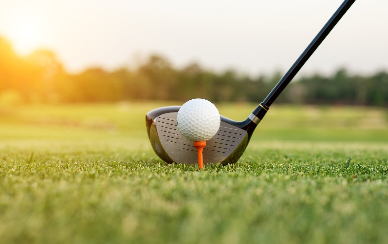 Golf club and ball in grass with sunlight. Close up at golf club and golf ball.