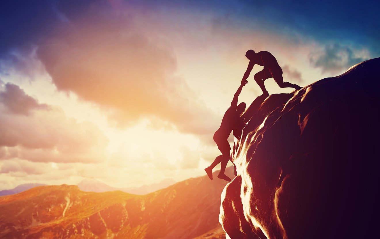 Hikers climbing on rock, mountain at sunset, one of them giving hand and helping to climb. Help, sup