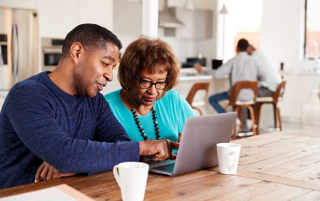 Middle aged black man helping his mother use a laptop computer at home, close up