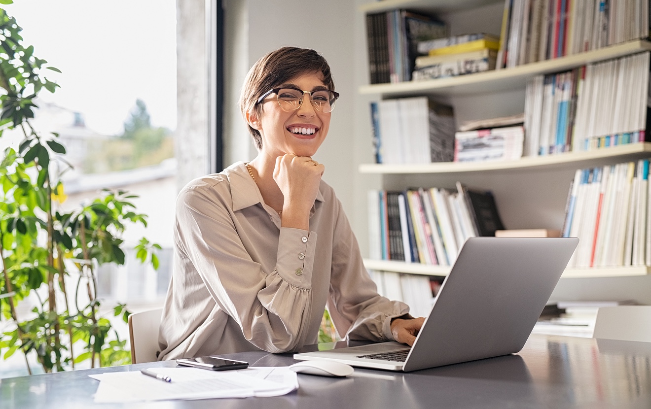 Successful young business woman sitting in creative office and looking at camera. Portrait of happy