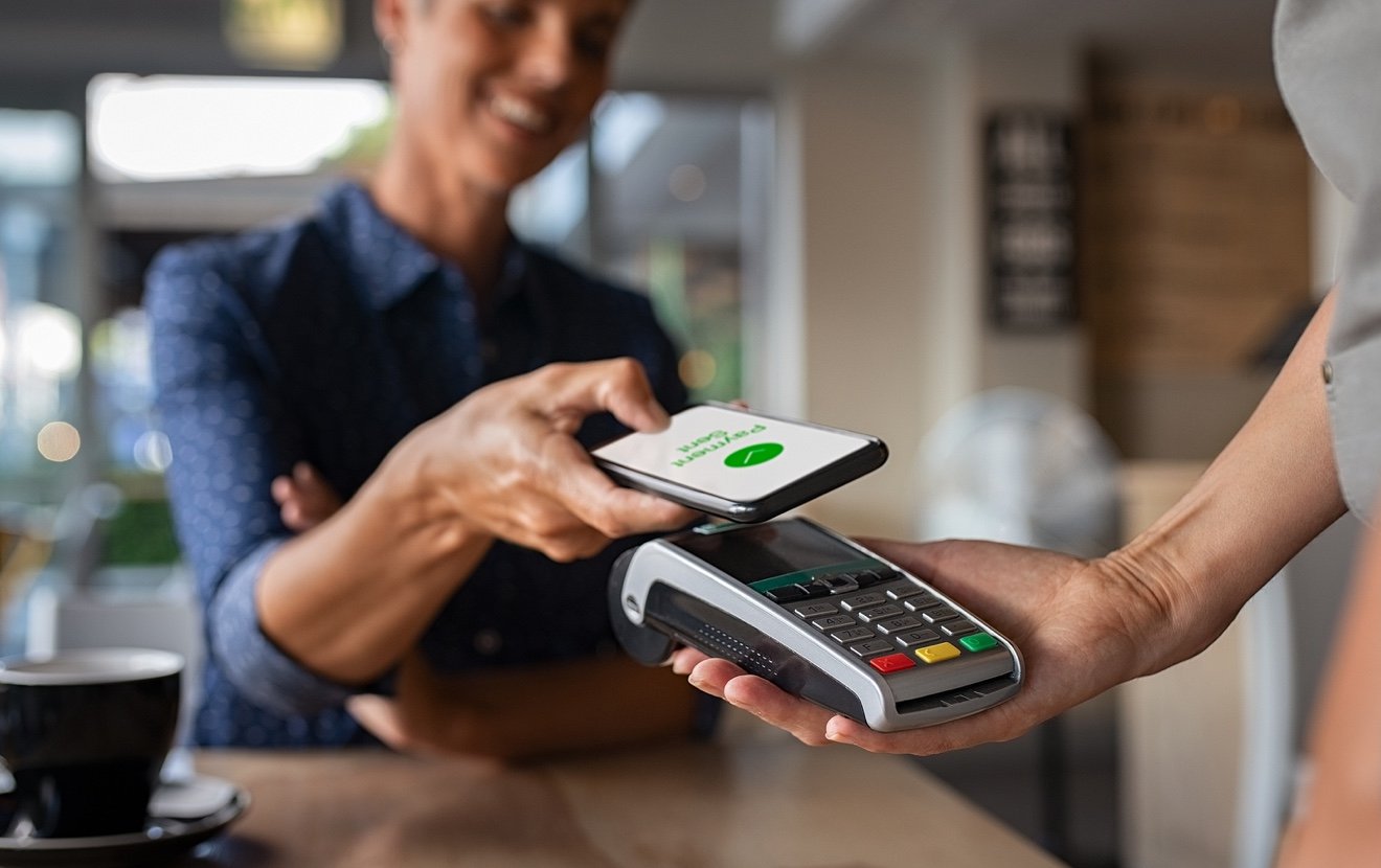 Woman paying bill through smartphone using NFC technology in a restaurant. Satisfied customer paying