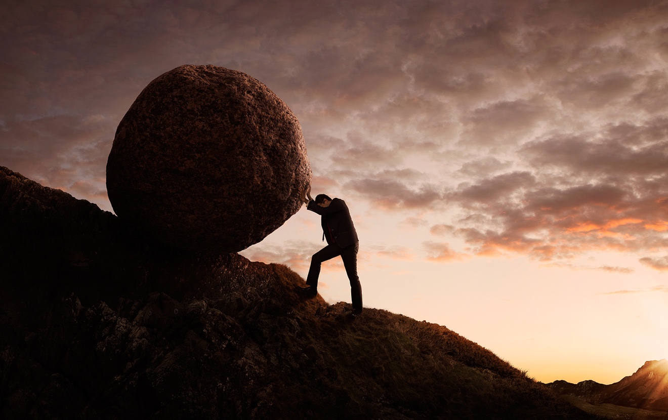 Business concept Young businessman pushing large stone uphill with copy space