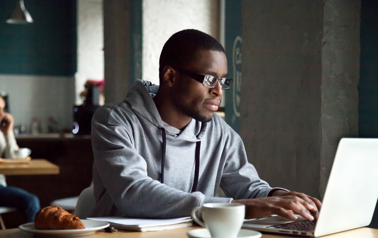 Serious Millennial African-american Man Using Laptop Sitting At Cafe Table, Focused Black Casual Guy