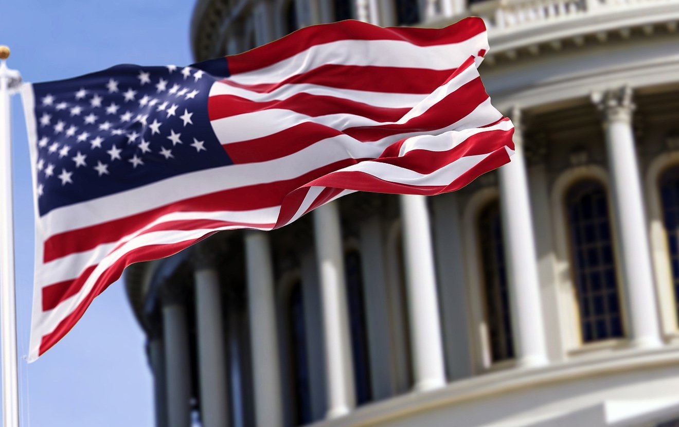 The Flag Of The United States Of America Flying In Front Of The Capitol Building Blurred In The Back