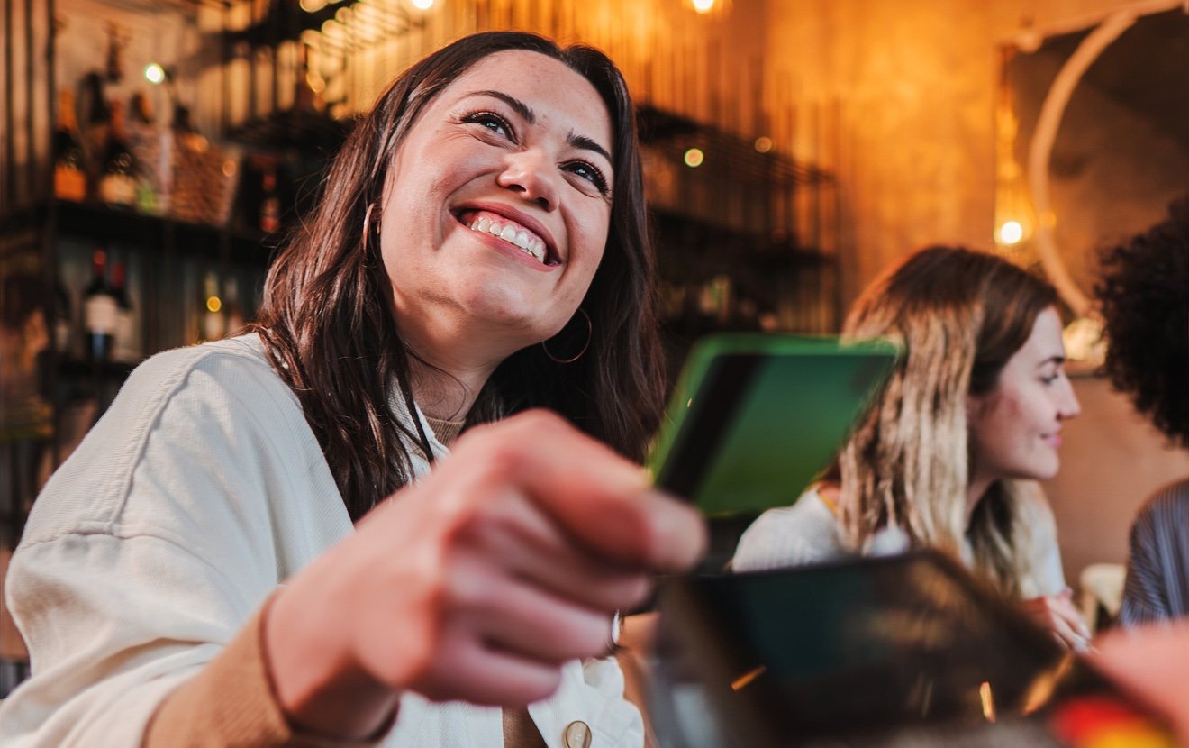 Vertical Portrait Of Happy Young Woman Paying Bill With A Contactless Credit Card In A Restaurant. C