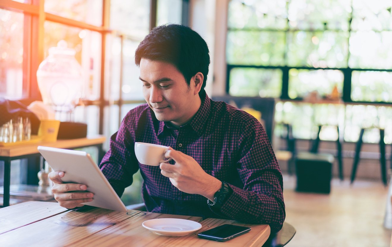 Young Asian Handsome Businessman Smiling While Reading His Tablet