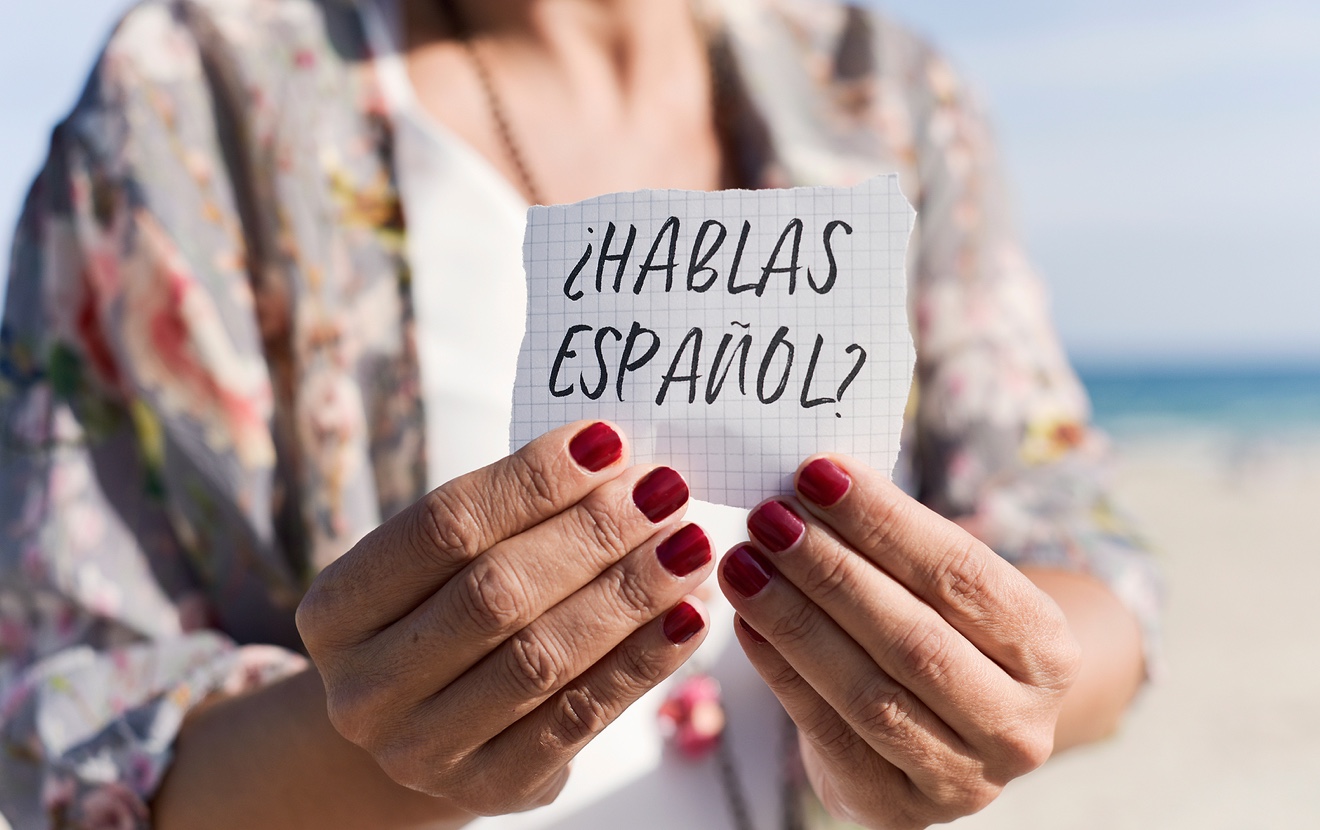closeup of a caucasian woman outdoors showing a piece of paper with the question hablas espanol, do