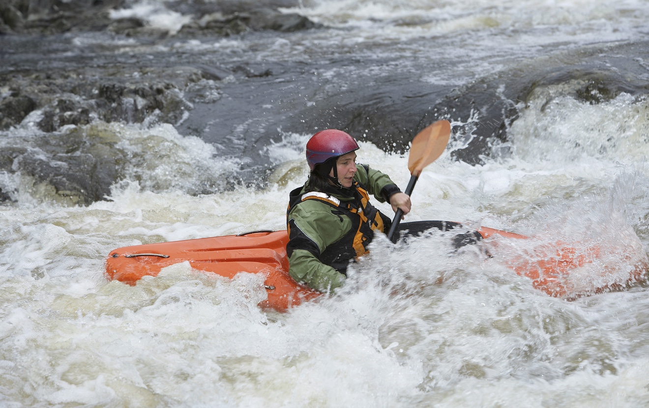 Side view of a woman kayaking in rough river